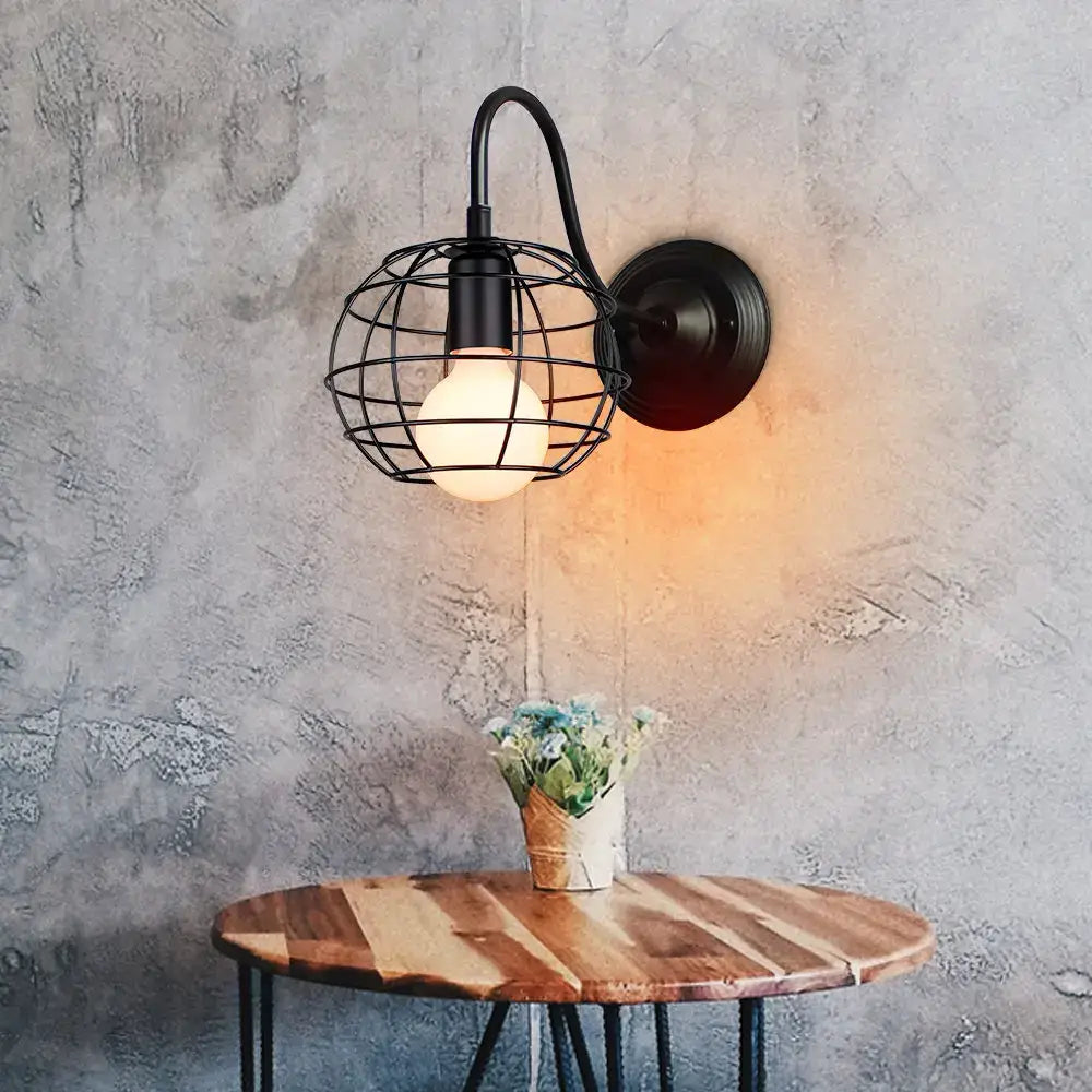 Black wrought iron wall sconce with a spherical wire cage housing an exposed bulb decorbites industrial iron wall fixture