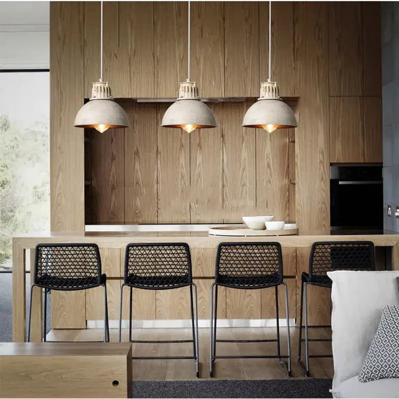 Three industrial loft chandelier pendant lights with concrete shades and copper fixtures hanging above wooden kitchen island