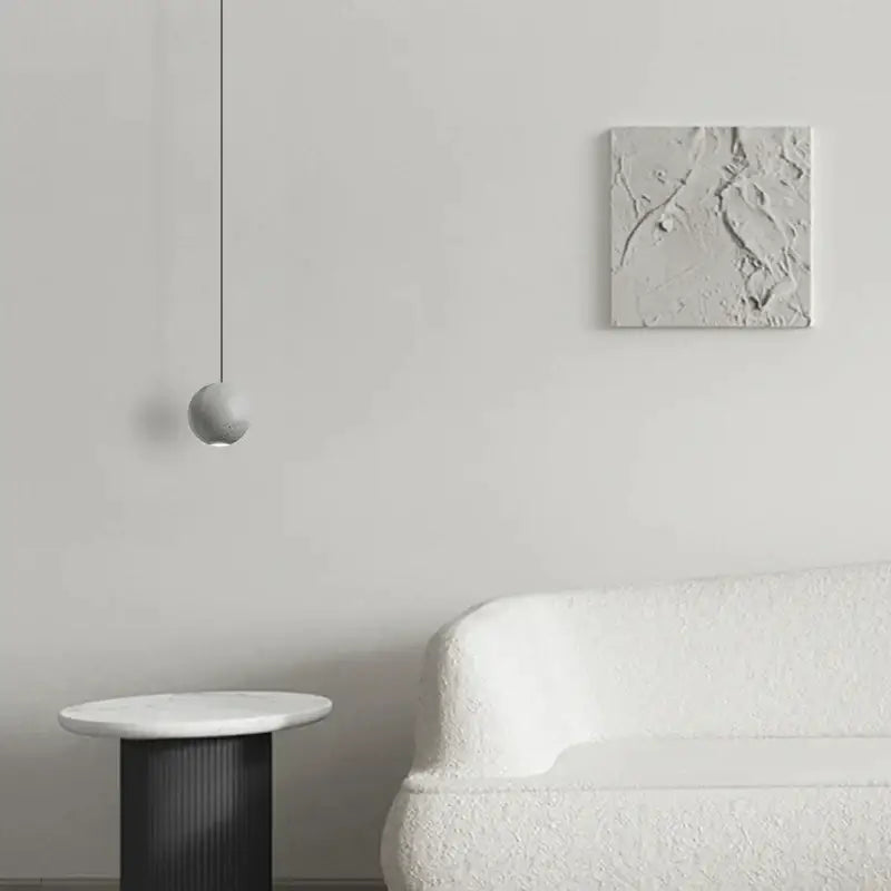Minimalist spherical pendant lamp with matte gray textured decorbites cement surface suspended by thin black cord