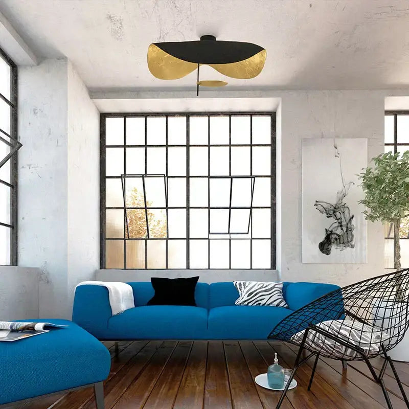 Blue upholstered sofa with black and zebra-print pillows under industrial retro gold and black decorbites flying saucer hat ceiling lamp