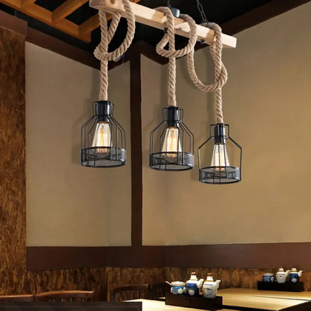 Three black metal cage pendant lights with exposed bulbs suspended by thick beige hemp rope chandelier from wood beam