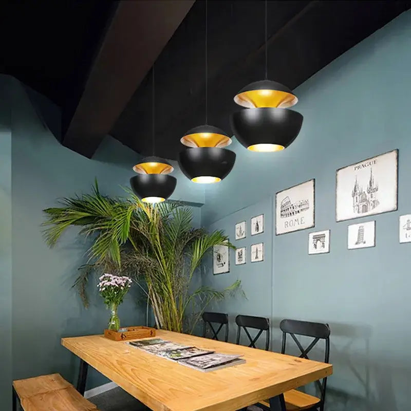 Industrial style led matte black pendant light with gold bowl-shaped design hanging above wooden dining table