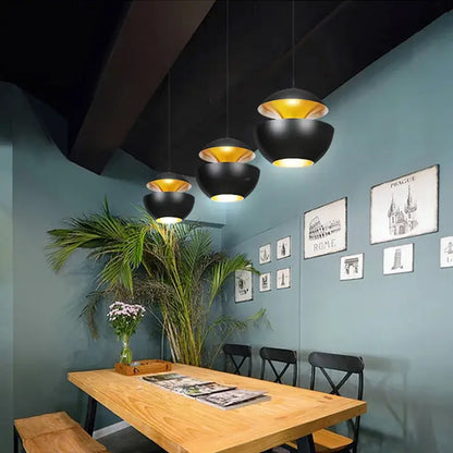 Industrial style led matte black pendant light with gold bowl-shaped design hanging above wooden dining table