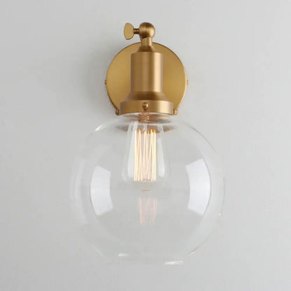 Industrial vintage wall sconce with a clear glass globe, brass-finished metal base, and exposed filament bulb for decorbites