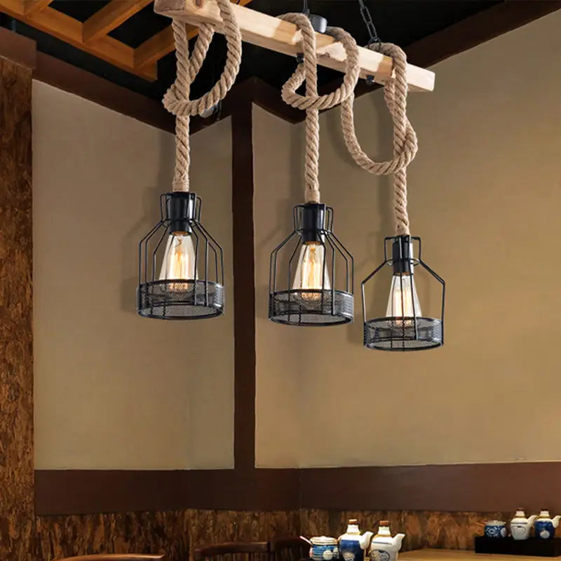 Three black metal cage pendant lights with exposed bulbs suspended by beige rope from wooden beam for restaurants