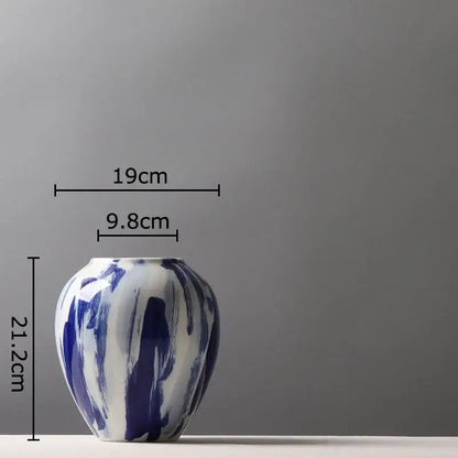 A ceramic vase with a glossy white base and bold ink style blue brushstroke flowers for living room decor