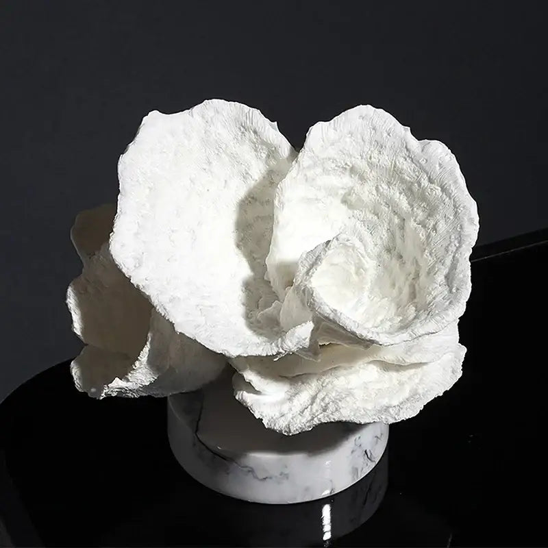 A sculpted white paper rose with layered petals on a marble base displayed alongside intricate pink glossy coral resin ornaments
