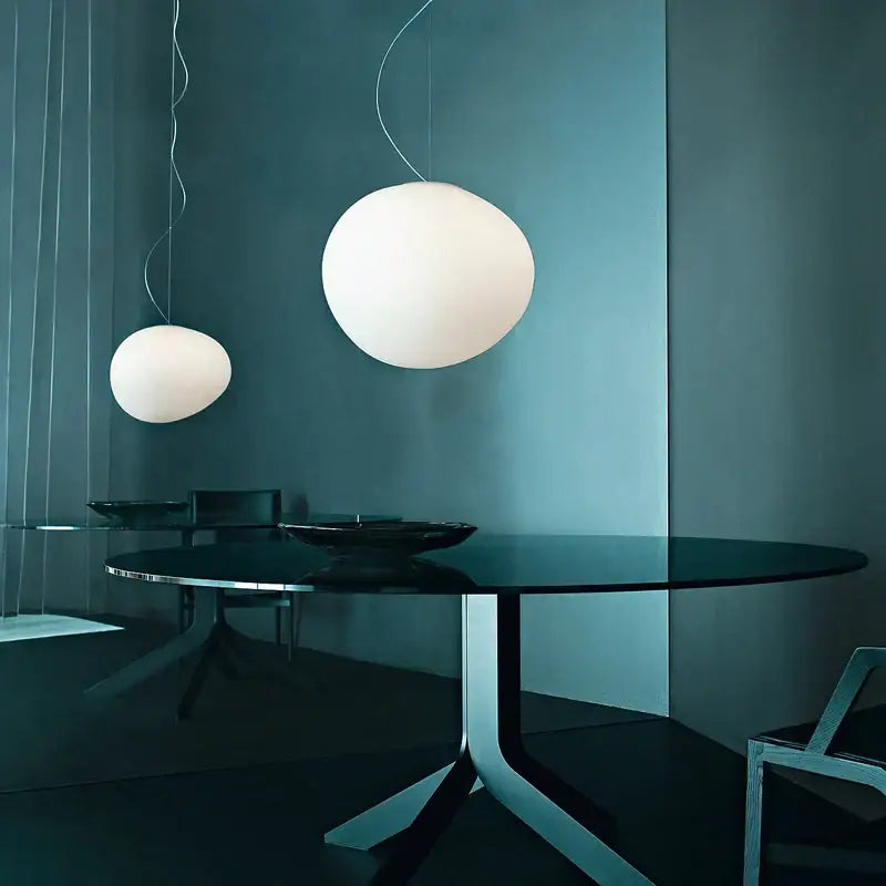 Two white spherical bubble glass pendant lamps hang above a dark glass table in italian style kitchen decorbites gregg pendant lamp