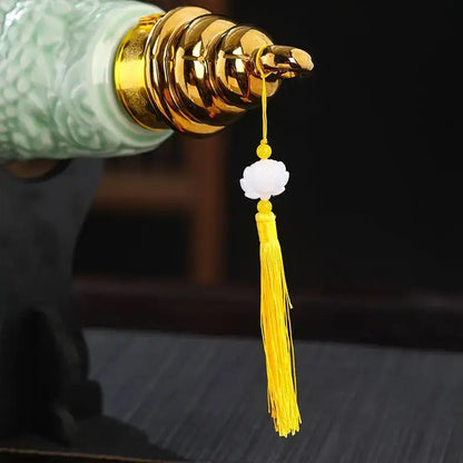 Delicate white jade flower pendant with golden bead and yellow tassel on a ceramic wine bottle dining room decor