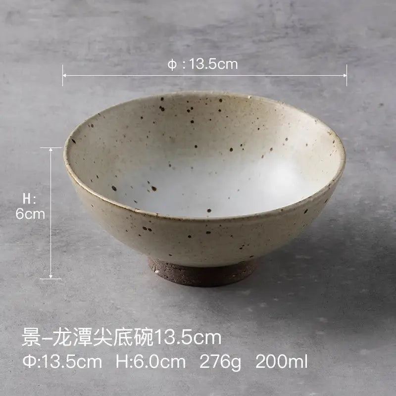 A beige and brown handmade ceramic rice bowl with dark speckles and wide rim for dining room use