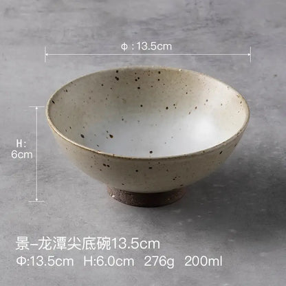 A beige and brown handmade ceramic rice bowl with dark speckles and wide rim for dining room use