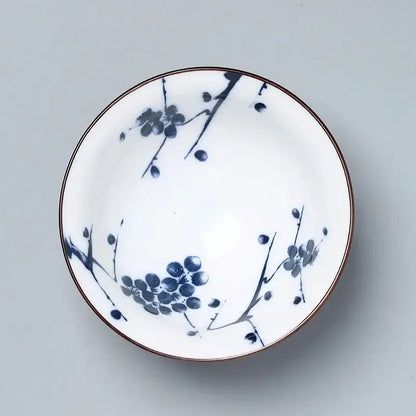 A white decorbites ceramic kung fu tea bowl with blue plum blossom patterns and a thin brown rim for dining room use