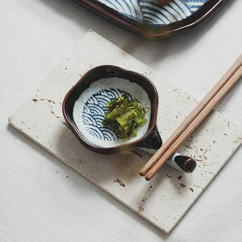 A dark brown ceramic japanese porcelain dipping bowl with blue wave patterns holding green pickled vegetables for decorbites dining