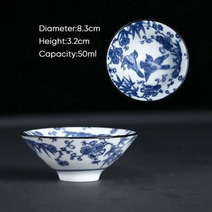 A delicate white ceramic kung fu tea cup with blue floral and bird motifs and a subtle black rim, perfect for tea