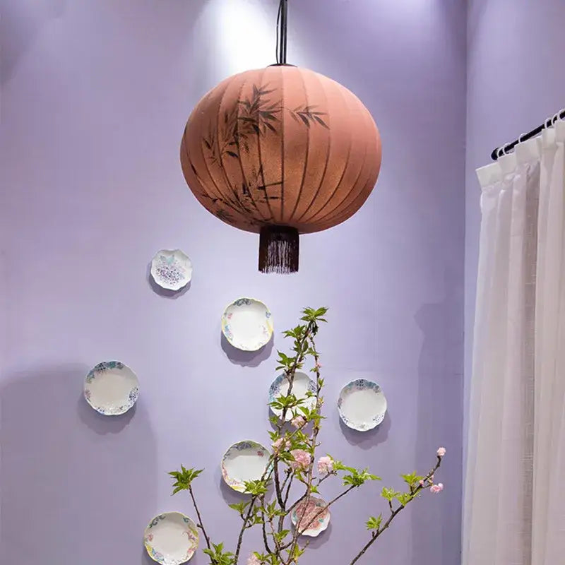 A peach-colored fabric japanese lantern painting with black bamboo leaf designs and dark fringe for dining room light