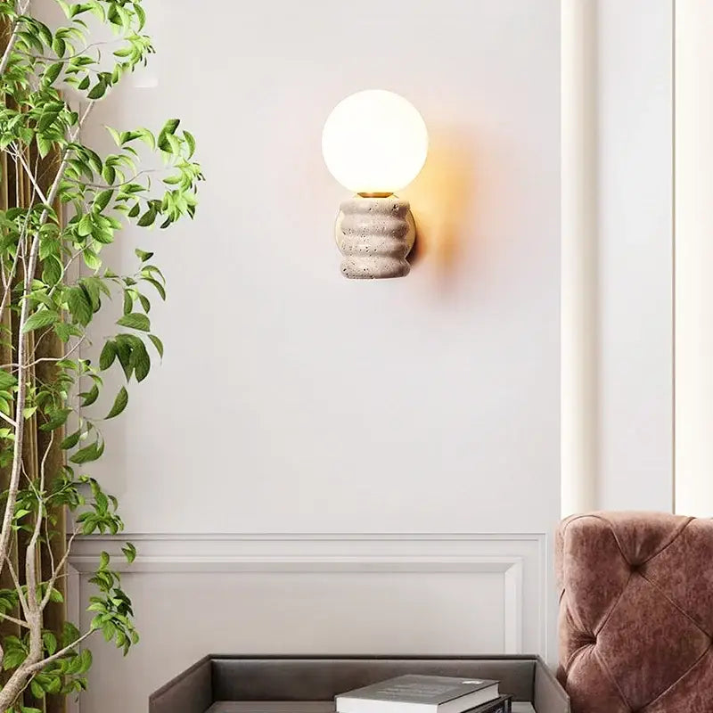 A warm spherical glass bulb led wall lamp mounted on a textured japanese travertine concrete base for bedroom use