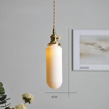 A warm-toned vertically ribbed glass pendant light with a polished copper finish metal fixture and twisted cord