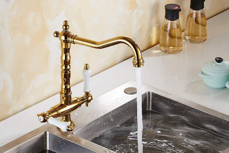 Gold brass single hole kitchen faucet with 360 degree swivel, ornate design, white ceramic handles, and curved spout