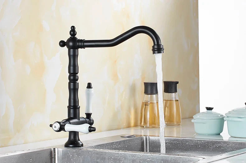 Black matte single hole kitchen faucet with white ceramic handles and curved spout mounted above stainless steel sink