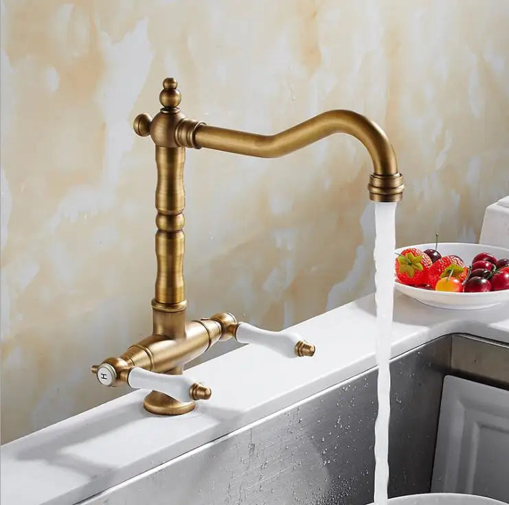 Antique brass single hole kitchen faucet with white ceramic handles curved spout and water flowing from nozzle