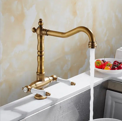 Antique brass single hole kitchen faucet with white ceramic handles curved spout and water flowing from nozzle