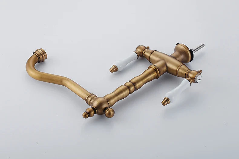 Antique brass finished single hole kitchen faucet with two white ceramic handles and ornate turned spout design