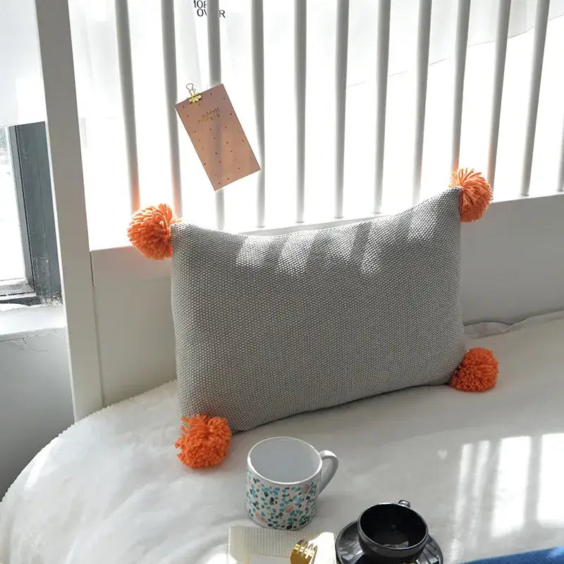 Gray textured knit cushion cover with bright orange pom-poms by decorbites for stylish living room decor