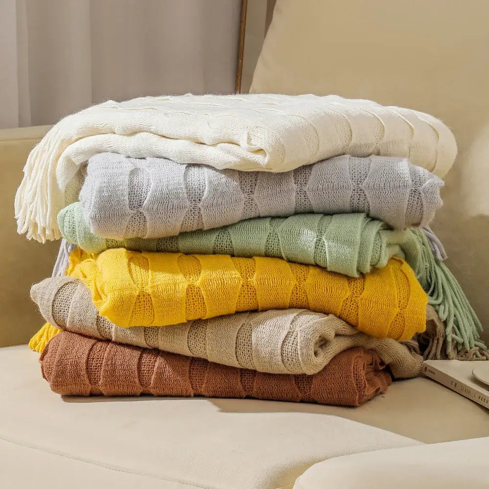 Stack of cozy decorbites knitted geometric throw blankets in soft pastel earthy tones with textured knit softness