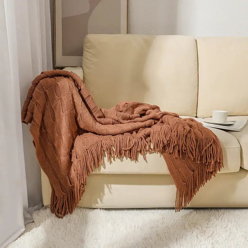 A cozy rust-colored decorbites knitted geometric throw blanket with cable knit texture and long fringe for bedroom decor