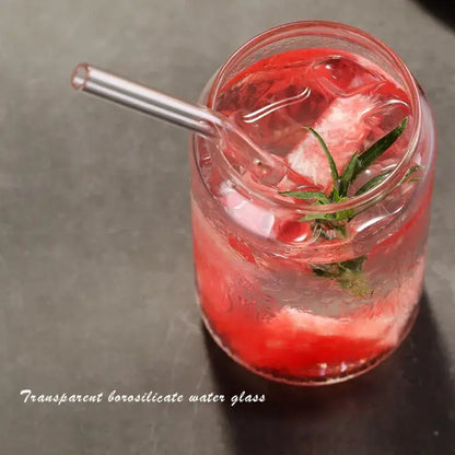 Transparent borosilicate large can shape beer glass cup filled with red beverage and ice garnished with green herb