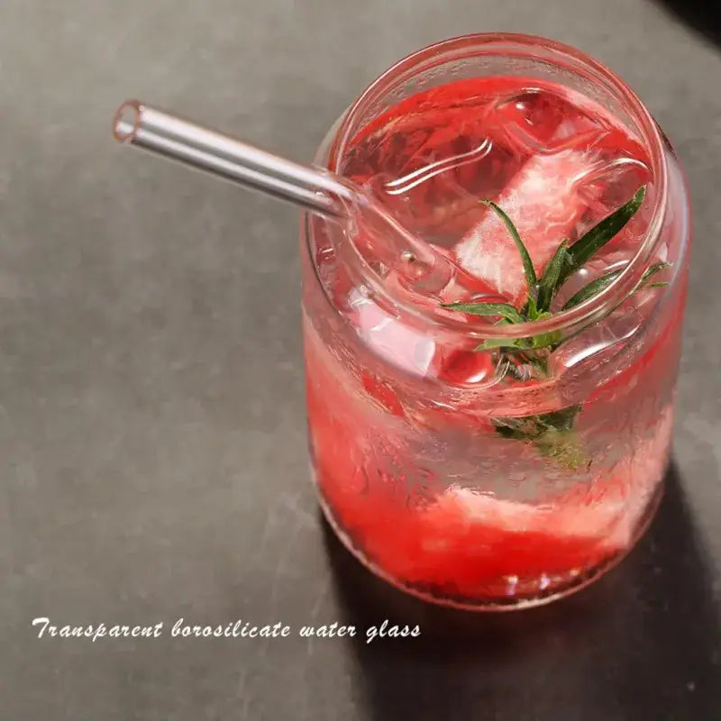 Transparent borosilicate large can shape beer glass cup filled with red beverage and ice garnished with green herb