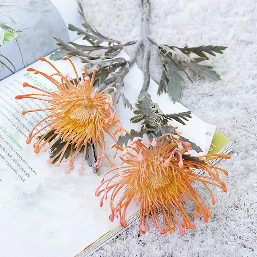 Lavender and orange artificial crab claw branch with orange and yellow protea flowers on an open book decorbites artificial crab