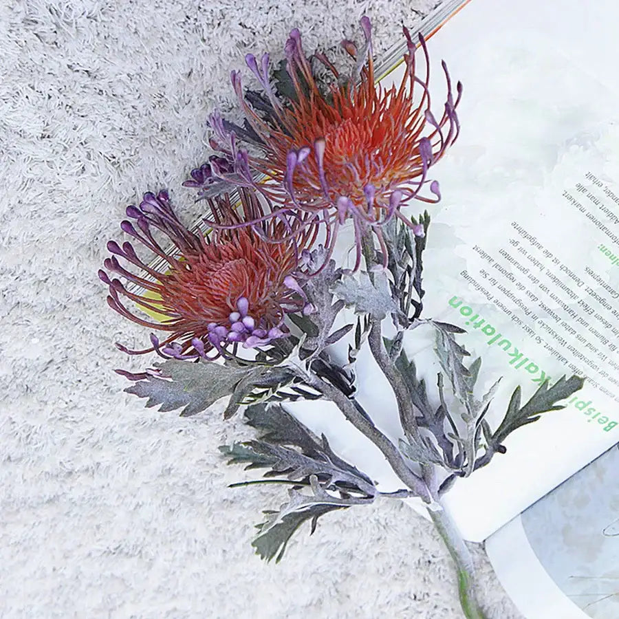 A vibrant artificial crab claw branch with fiery orange and deep purple petals and silvery green leaves for decorbites decor
