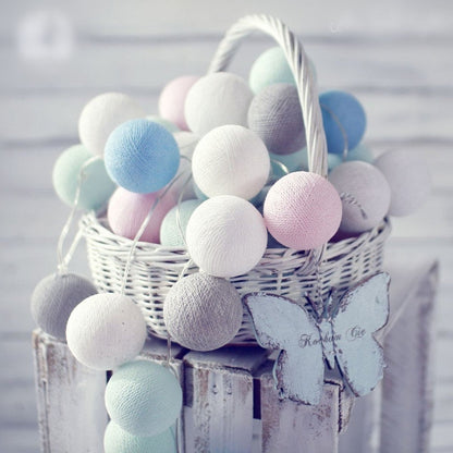 Led cotton ball lights garland in pastel colors displayed in white wicker basket with wooden butterfly accents