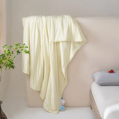 A soft pale yellow silk-like throw blanket draped over a bedhead for decorbites cool fiber summer cooling quilt