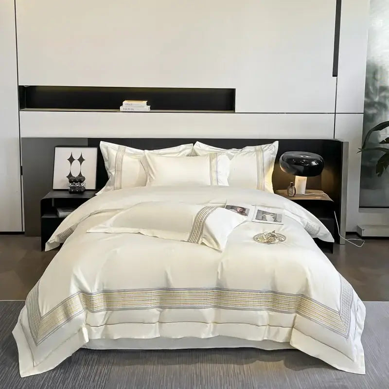 Cream-colored satin bedding set with gold and silver striped egyptian cotton embroidery along edges in bedroom