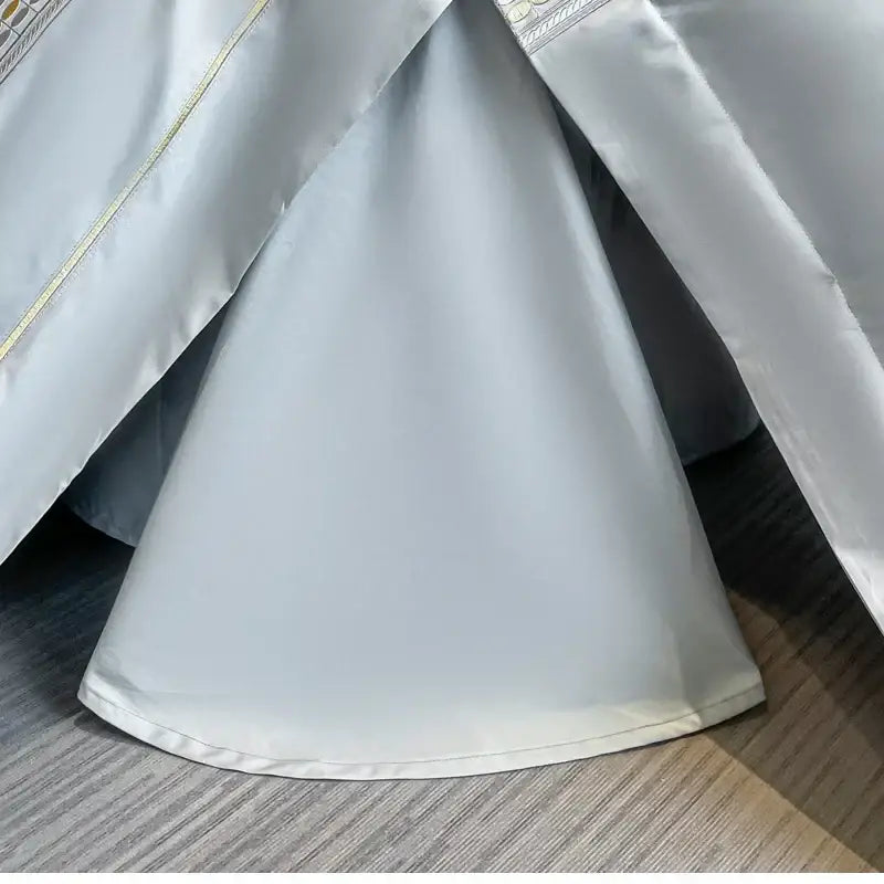 Light gray satin bed skirt with subtle gold trim paired with light blue egyptian cotton embroidery duvet cover bedding set