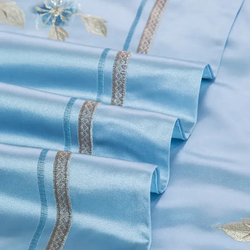 Light blue satin pillowcases with delicate floral embroidery and silver stripes in a 200s cotton embroidery bedding set