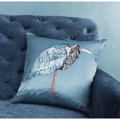 A plush teal silk throw pillow cover featuring an intricately embroidered light blue heron with detailed feathers
