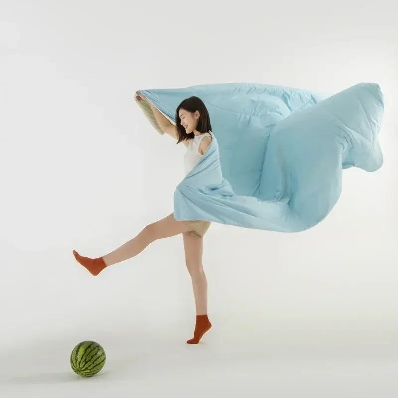 Light blue and white decorbites cooling fabric summer blanket flowing dynamically around a woman’s body