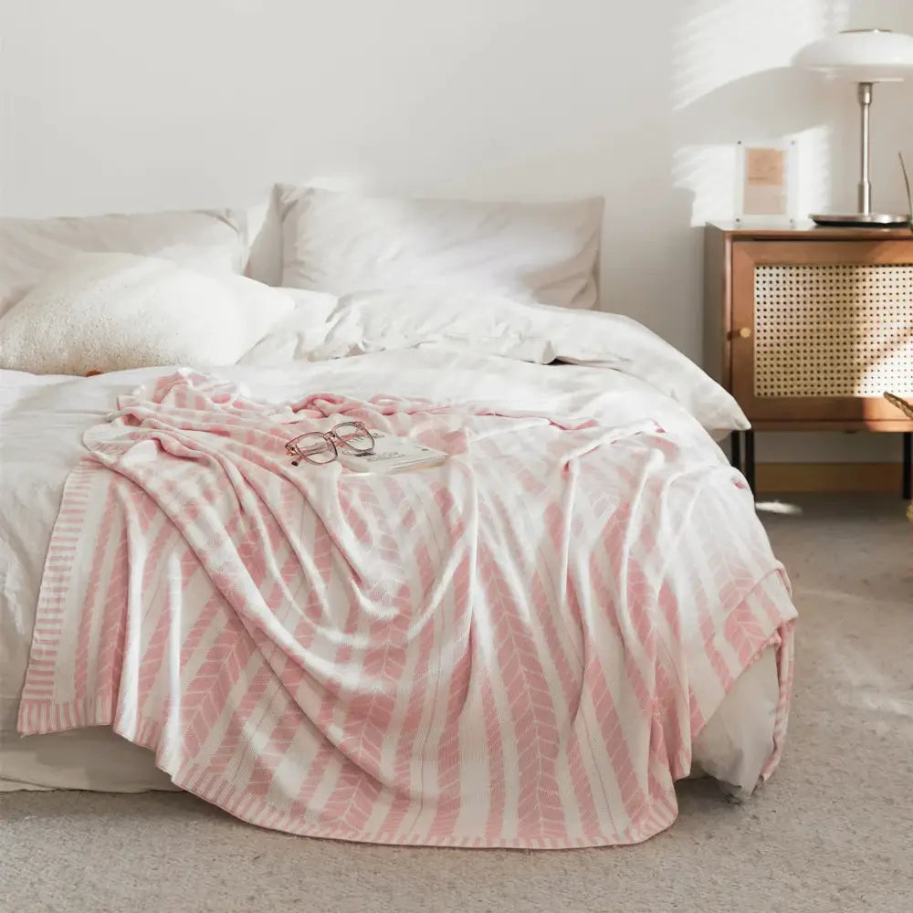 A soft pink and white striped bamboo knitted cooling blanket with light green leaf pattern draped over a bed decorbites cooling blanket
