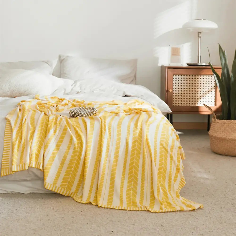 A cozy yellow and white striped bamboo knitted cooling blanket with a chevron pattern draped over a bed