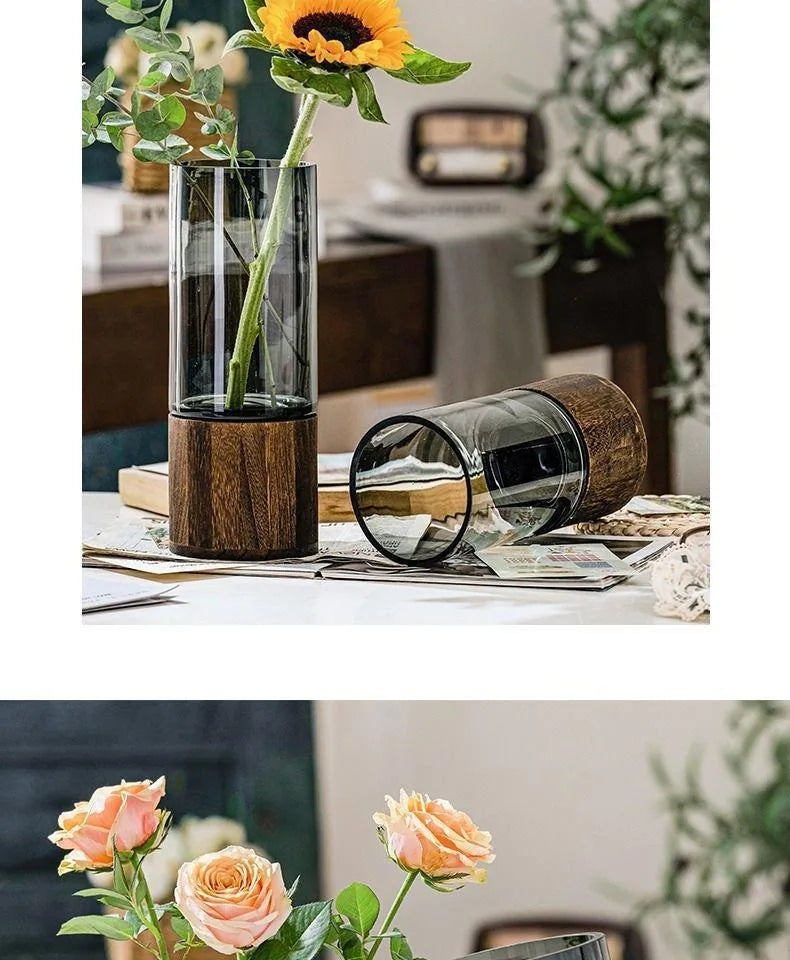 Tall transparent glass vase with dark wood base holding single sunflower for living room table decoration