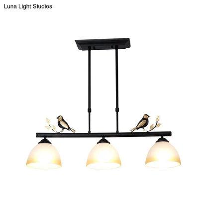 Black wrought iron pendant light with three milky glass shades and decorative bird motifs on central bar
