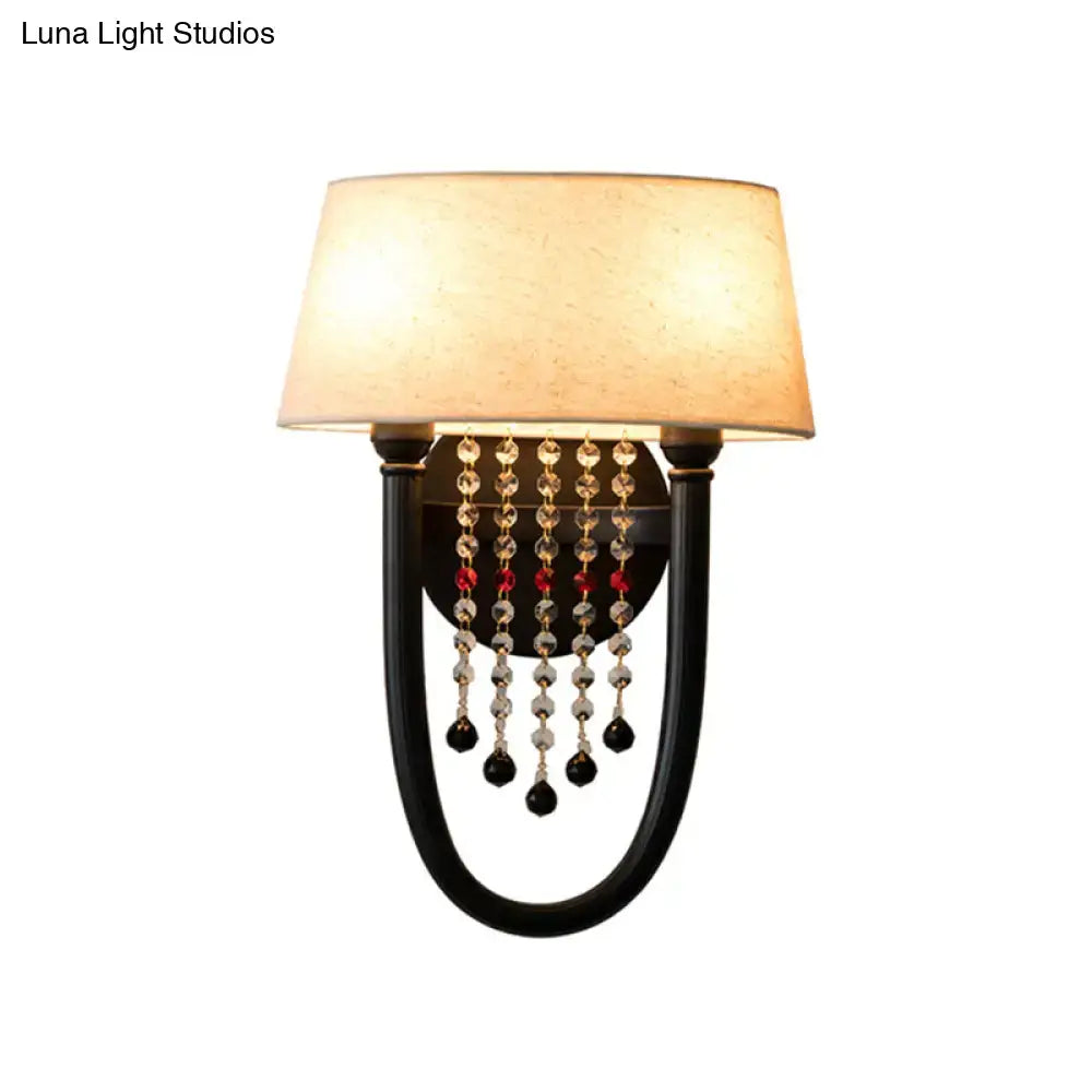 Elegant black wrought iron wall lamp with beige fabric drum shade and crystal bead detail for bedroom use
