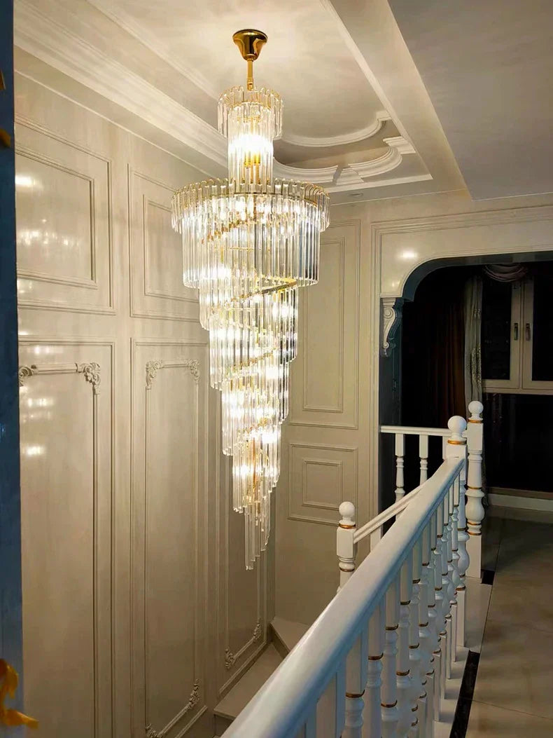 A long crystal staircase gold chandelier with cascading clear glass rods and a gold finish, ideal for a hotel hall