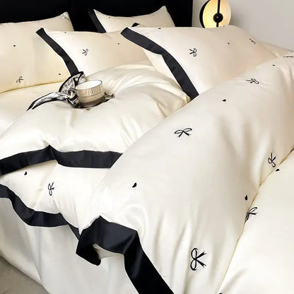 Luxury cream-colored satin bedding set with black ribbon trim and embroidered bow motifs from decorbites ice silk collection