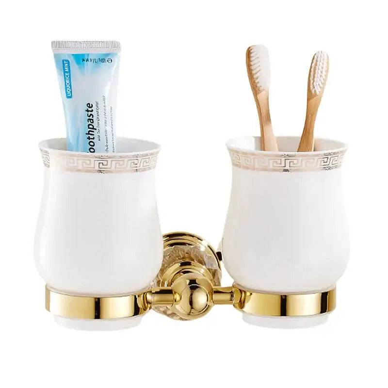 White ceramic toothbrush holders with gold accents and greek key pattern on brass wall bracket for luxury bath hardware