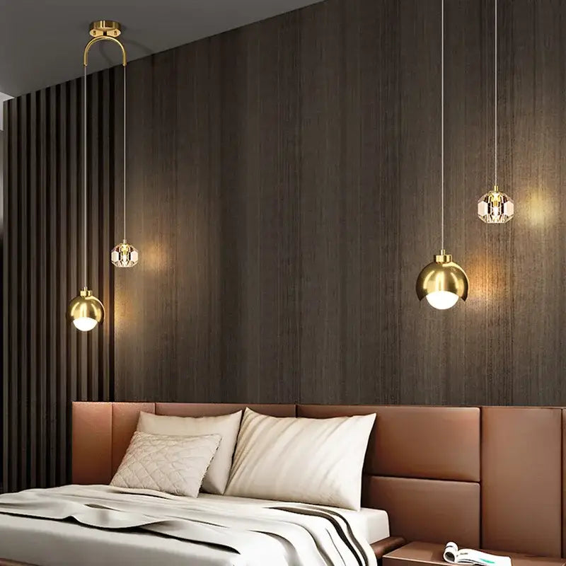 Three elegant gold-toned decorbites glass ball pendant lights with crystal accents hang above a modern bed