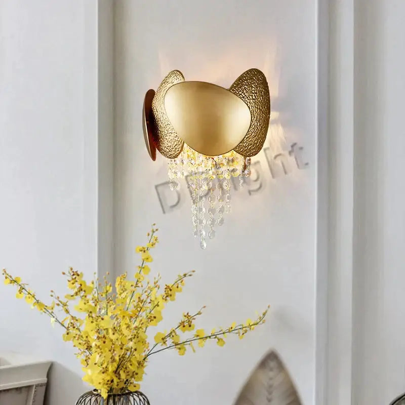 Gold-toned wall sconce with textured egg-shaped metal plates and crystal droplets complements a led ceiling chandelier